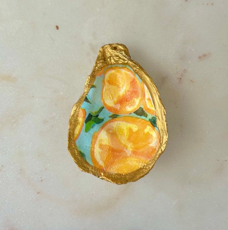 May include: A gold-painted oyster shell with a blue and white pattern of oranges. The shell is a decorative dish or trinket.