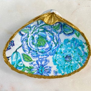 May include: A white ceramic seashell dish with a gold rim and a blue and white floral pattern.