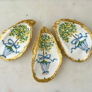 May include: Three oyster shell dishes with gold rims and painted lemon tree designs. Each dish features a blue and white planter with a lemon tree and yellow lemons.