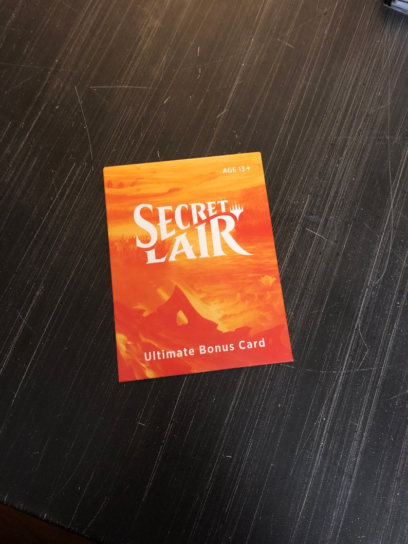 May include: Orange and yellow Secret Lair Ultimate Bonus Card with the text "Secret Lair" and "Ultimate Bonus Card".