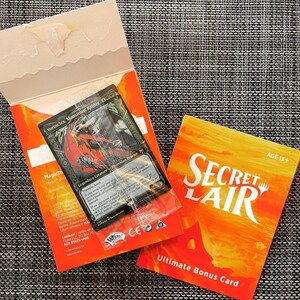May include: A Secret Lair Ultimate Bonus Card featuring a black and white illustration of a creature with a red background. The card is in a clear plastic sleeve and is surrounded by a bright orange background with the text "Secret Lair" and "Ultimate Bonus Card".