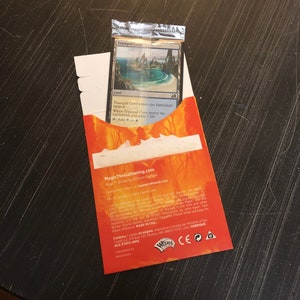 May include: A red and orange Magic: The Gathering booster pack with a foil card inside. The card is a land card called "Tranquil Cove". The back of the booster pack has the Magic: The Gathering logo and website address.