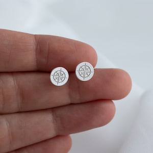 May include: A pair of silver compass stud earrings. The earrings are small and round, with a compass design in the center.