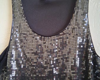 May include: A black sequined tank top with a scoop neckline. The top is covered in small, square, shiny sequins that reflect light. The H&M brand label is visible at the neckline. The garment is hanging on a white hanger.