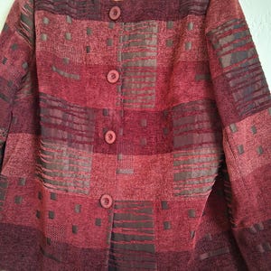 May include: A burgundy blazer with a textured pattern and four matching buttons. The jacket features a round neckline and long sleeves. The label reads "BEA".