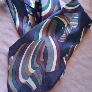 May include: A navy blue tie with a repeating abstract pattern of curved lines in shades of white, brown, purple, teal, and blue. The tie is made of a smooth fabric and is displayed on a light purple surface.