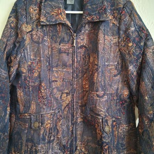 May include: A navy blue jacket with a patterned design in shades of brown, gold, and red. The jacket has a zipper closure, two front pockets with decorative buttons, and a collar. The brand name "TANJAY" is visible on the label.