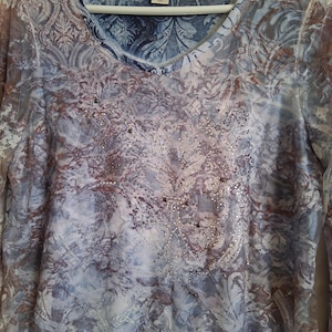May include: A long-sleeve top with a blue, white, and brown paisley and floral pattern. The shirt features a scoop neckline, a Christopher & Banks brand label, and a central embellishment of small, clear, and dark-toned decorative studs.