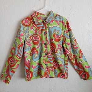 May include: A green, orange, pink, and blue patterned button-up shirt with long sleeves. The shirt has a collar and a button closure. The brand label reads "Liz Claiborne New York".