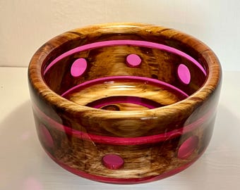 May include: A wooden bowl with a pink resin finish. The bowl has a unique design with holes and stripes.