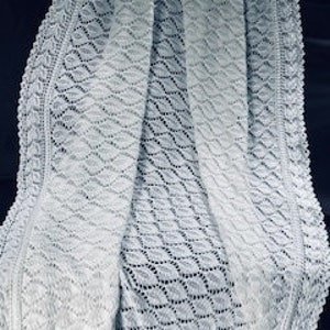 Pode incluir: Um cobertor de bebé branco de crochê com um padrão delicado de folhas. O cobertor é feito com um fio fino e tem uma sensação macia e arejada.