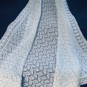 May include: A white, open-weave shawl with a delicate leaf pattern. The shawl is draped, showcasing its intricate design and texture. The fabric appears soft and lightweight, suitable for layering.