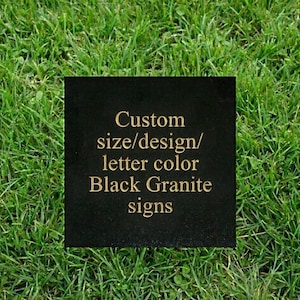 May include: A black granite sign with gold lettering that reads "Custom size/design/letter color Black Granite signs." The sign is square and set against a background of green grass.