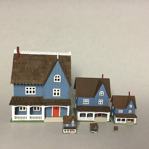 May include: Five miniature houses made of wood, painted blue with brown roofs. The houses are arranged in order of size, with the largest house in the back and the smallest house in the front. The houses have white trim and windows, and some have porches.