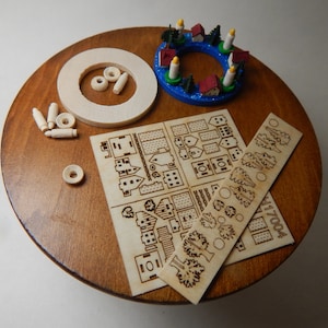 May include: A wooden craft kit for building a miniature Christmas village. The kit includes a blue and red Advent wreath, a sheet of laser-cut wooden houses, trees, and other details, and a ruler with the number "4170004".