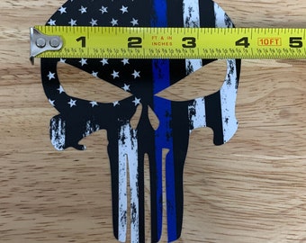 May include: A black and white skull with a blue line running down the center. The skull is decorated with an American flag pattern. A measuring tape is placed across the top of the skull, showing a measurement of 3 inches.
