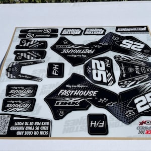 May include: Black and white motorcycle graphics kit with the words "Fast House" and "Piston Bones" printed on the decals. The kit includes a number plate with the number "25" printed on it.