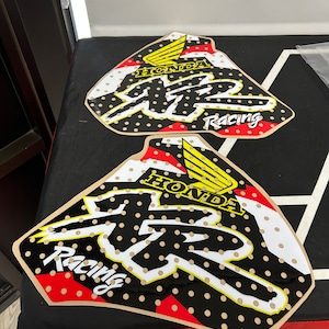 May include: Two black and white motorcycle graphics with red and yellow accents. The graphics feature the word "Honda" and the letter "R" with the word "Racing" underneath. The graphics have a dotted pattern.