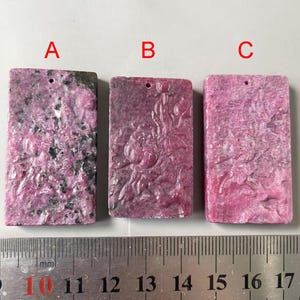 May include: Three rectangular pink and grey gemstone pendants with a hole at the top for hanging. The pendants are approximately 3.8 cm long and 1.9 cm wide. The pendants are labelled A, B, and C.