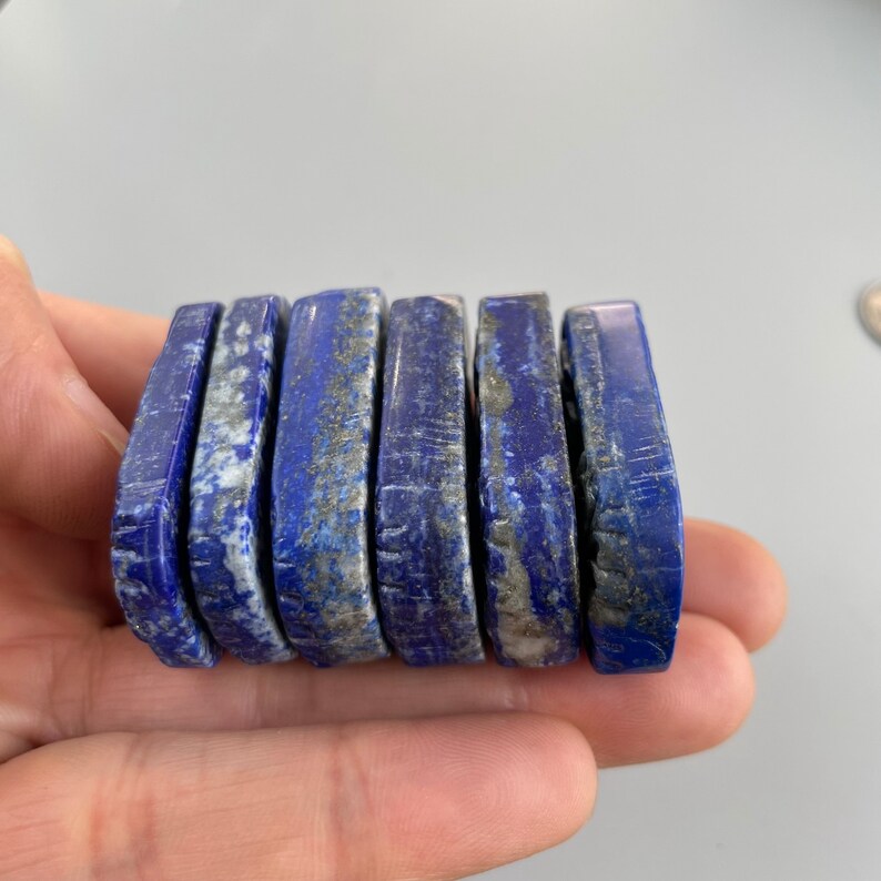 May include: A stack of six smooth, rectangular lapis lazuli stones with a deep blue color and white and gold flecks.