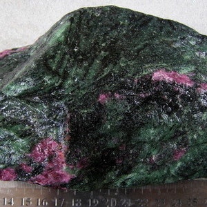 Puede incluir: Una piedra preciosa grande, rugosa, verde y rosa con un patrón moteado verde oscuro y negro. La piedra preciosa mide aproximadamente 10 cm de largo.