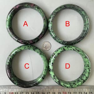 Könnte beinhalten: Vier grüne, schwarze und rosafarbene Edelstein-Armbänder. Die Armbänder sind quadratisch auf einer weißen Oberfläche angeordnet. Die Armbänder sind mit A, B, C und D beschriftet.