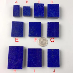 Può includere: Una collezione di dieci pietre rettangolari di lapislazzuli di varie dimensioni, disposte su una superficie bianca. Le pietre sono di un blu intenso con sottili macchie dorate, che ne evidenziano la bellezza naturale. Una moneta è inclusa per il confronto delle dimensioni.