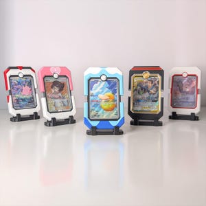 May include: Five colourful card display stands, each holding a different trading card. The stands are white, black, red, pink, and blue, with a small circular accent at the top. The cards feature various characters and artwork.
