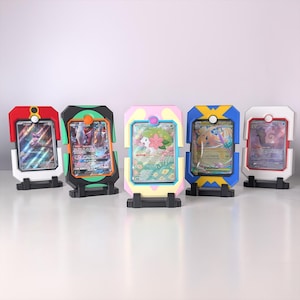 May include: Five colourful card display stands. Each stand holds a trading card and features a unique colour scheme: red, black, pink, blue, and white. The stands have a rectangular frame with a circular accent at the top and a black base.