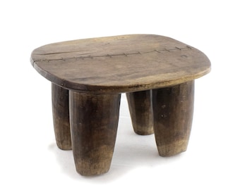 May include: A dark brown wooden stool with four legs. The top of the stool is slightly rounded and has a stitched seam across the center.