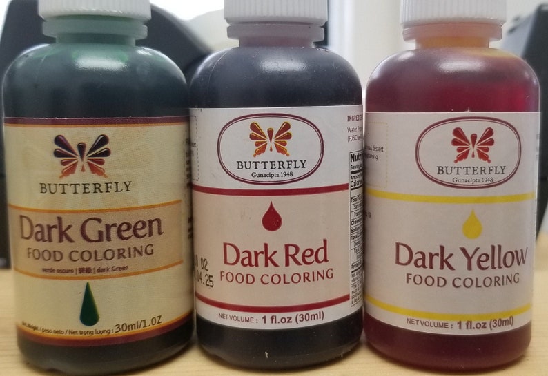 May include: Three glass bottles of food coloring, each with a different color: dark green, dark red, and dark yellow. Each bottle has a label with the brand name "Butterfly" and the text "Food Coloring". The bottles are 1 fluid ounce each.