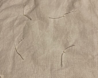 May include: A close-up of a beige fabric with a subtle pattern of small, embroidered loops. The fabric has a slightly textured surface.