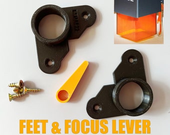 May include: Two black 3D printed feet and a focus lever for an XTOOL D1 3D printer. The feet have a round hole in the center and the lever is a small orange piece with a hole in the center. There are also four small gold screws.