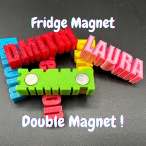 May include: A set of colorful 3D printed fridge magnets with the names "Laura", "Dmitri", and "John" on them. The magnets are attached to a green double magnet with two silver magnets on the back.
