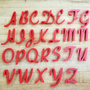 May include: Red wooden letters of the alphabet in a cursive font. The letters are arranged in alphabetical order on a wooden surface.