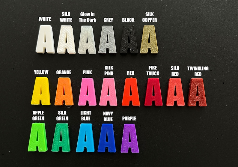 May include: A chart of 18 different colors of plastic letters, each letter is the letter 'A'. The colors are white, silk white, glow in the dark, grey, black, silk copper, yellow, orange, pink, silk pink, red, fire truck, silk red, twinkling red, apple green, silk green, light blue, navy blue, and purple.