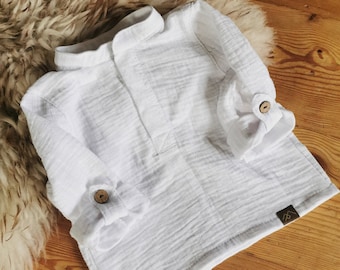 May include: A white long-sleeve shirt made of textured fabric featuring a mandarin collar, a partial front button placket, and sleeves with roll-up tabs secured by brown wooden buttons. A small dark rectangular brand tag is on the lower hem.