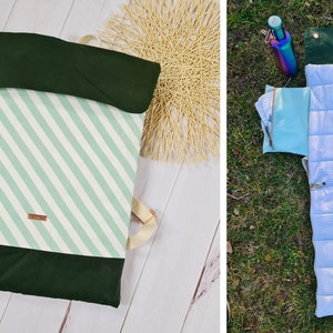 May include: A green and white striped travel pillow with a dark green outer layer and a zipper. The pillow is folded and laid flat on a white wooden surface. The pillow is also shown unfolded and laid flat on a green grassy surface.