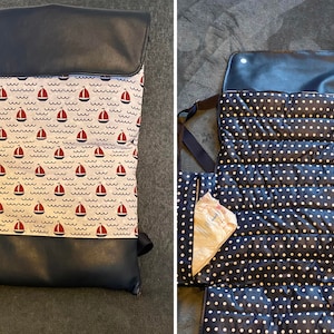 May include: A black and white polka dot changing mat with a black faux leather flap. The mat has multiple pockets and is folded open to reveal the interior. The mat is designed for changing babies.