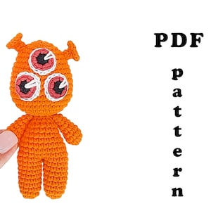May include: Crochet pattern PDF for a three-eyed orange amigurumi monster. The pattern includes instructions for making the monster's body, head, and eyes.