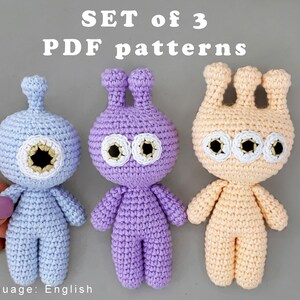 May include: Set of three crochet amigurumi patterns for making three different alien characters. The aliens are blue, purple, and peach in color. The patterns are available in English.