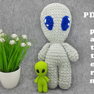 May include: A crochet pattern for a gray alien amigurumi toy with blue eyes. The pattern is available as a PDF download. The image also shows a smaller green alien amigurumi toy.