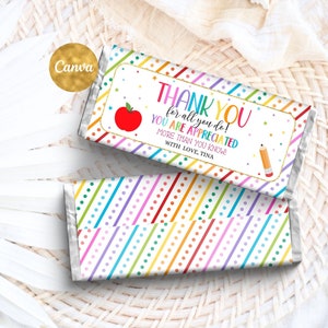 Pode incluir: Um embrulho de chocolate colorido com um padrão de listras arco-íris e bolinhas brancas. O embrulho tem um rótulo que diz "Obrigado por tudo o que você faz! Você é apreciado mais do que sabe! Com amor, Tina". Há uma maçã vermelha e um lápis amarelo no rótulo.