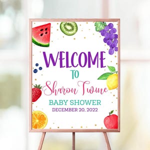 May include: A wooden easel holds a sign with the words "WELCOME TO Sharon Twine BABY SHOWER DECEMBER 20, 2022." The sign is decorated with watercolor illustrations of fruits, including watermelon, kiwi, grapes, strawberries, oranges, lemons, and apples.