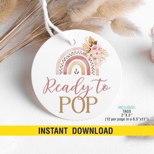 May include: A round, white tag with a watercolor rainbow design in shades of pink, orange, and brown. The rainbow is topped with a floral arrangement of beige and pink flowers. The text "Ready to POP" is written in brown and gold lettering. The tag is labeled "INCLUDED: TAGS 2"x2" (12 per page in a 8.5"x11")" and "INSTANT DOWNLOAD".