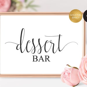 May include: A printable sign with a gold foil effect that says "dessert bar" in a cursive font. The sign is in a rose gold frame and is sitting on a white surface.