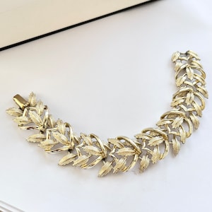 Puede incluir: Un brazalete dorado con un diseño de hojas. El brazalete está hecho de metal y tiene un aspecto delicado y femenino.
