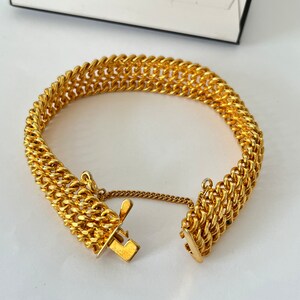 Puede incluir: Un brazalete de cadena de oro con una doble fila de eslabones entrelazados. El brazalete tiene un cierre de broche.