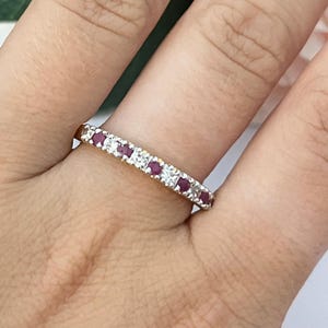 May include: A gold band ring featuring an alternating pattern of small round-cut red rubies and clear white diamonds set in a straight row across the top of the band. The metal has a polished finish and the stones are set securely in the metal channel.