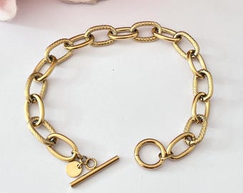 Puede incluir: Un brazalete de cadena dorado con un diseño de eslabón ovalado texturizado. El brazalete tiene un cierre de barra en T.